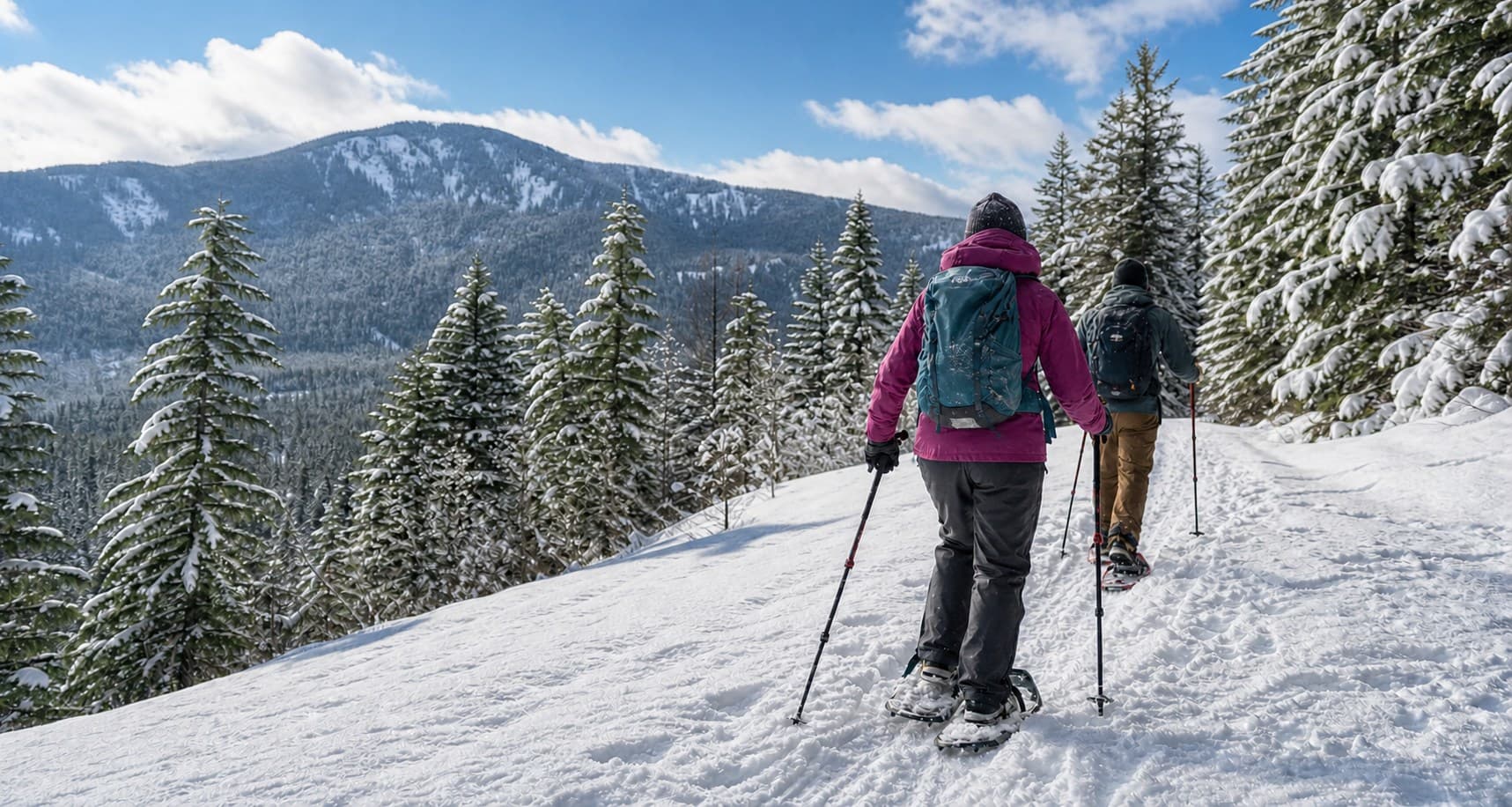 Two snowshoers traveling a snow-covered Cascade forest trail